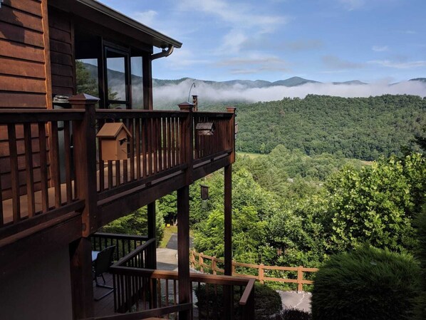 A wooden cabin with a balcony overlooking a forested valley and mountains.