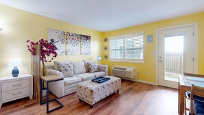 Una sala de estar con sofá, mesa de centro, mesita auxiliar con lámpara y un jarrón decorativo con flores.
