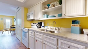 Cocina con gabinetes blancos, un lavamanos de acero inoxidable y una cafetera.