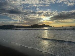 A beach with waves, a sunset, and distant mountains. - Where your dream vacation in Coco begins.... (Playas del Coco)
