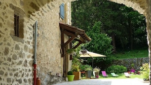 A stone building with a covered patio area, outdoor seating, and a view of a lush green landscape. - Maison d'Hôtes du Domaine Fournié (Tarascon-sur-Ariege)