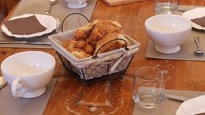 A breakfast setting with bread, pastries, and beverages on a wooden table. - Maison d'Hôtes du Domaine Fournié (Tarascon-sur-Ariege)