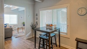 A dining area with a table and stools, a window with blinds, and a clock on the wall.