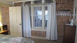 A bedroom with a brick wall, a window with curtains, a bed with a quilt, and a wooden dresser. - Historic Civil War house, great for family getaways.   (Gettysburg)