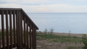 Une terrasse en bois donnant sur une plage, avec un rivage sablonneux et une végétation clairsemée.