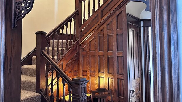 A wooden staircase with intricate railings and a chair at the bottom. - Spectacular Family Getaway!  (Gettysburg)