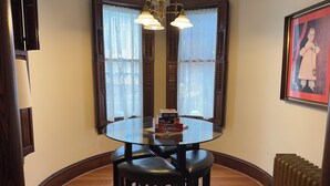 A dining area with a round glass table, two black chairs, lace curtains, a chandelier, and a framed picture on the wall. - Spectacular Family Getaway!  (Gettysburg)