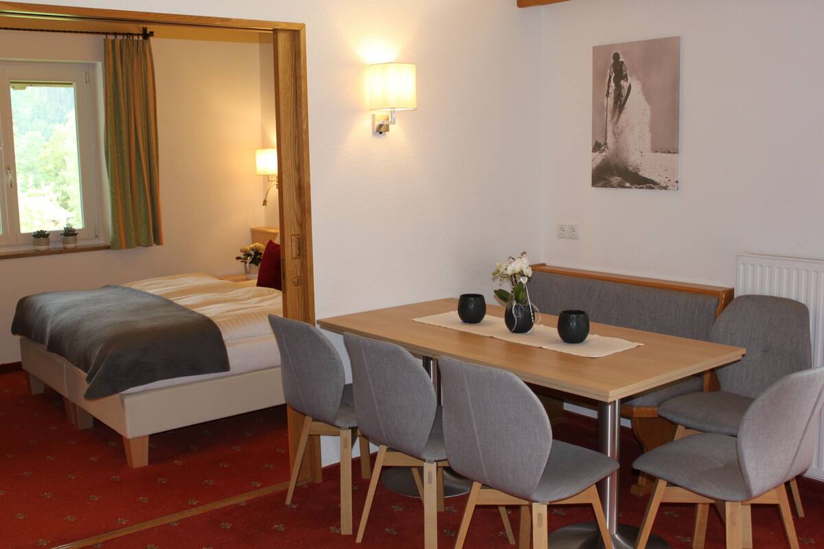 Hotellihuone, jossa on sänky, pöytä tuoleineen, lamppu ja taulu seinällä.