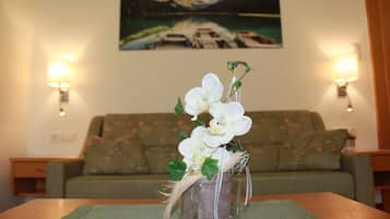 Una habitación con un sofá verde, una mesita con un florero de flores blancas y un cuadro de un lago en la pared.
