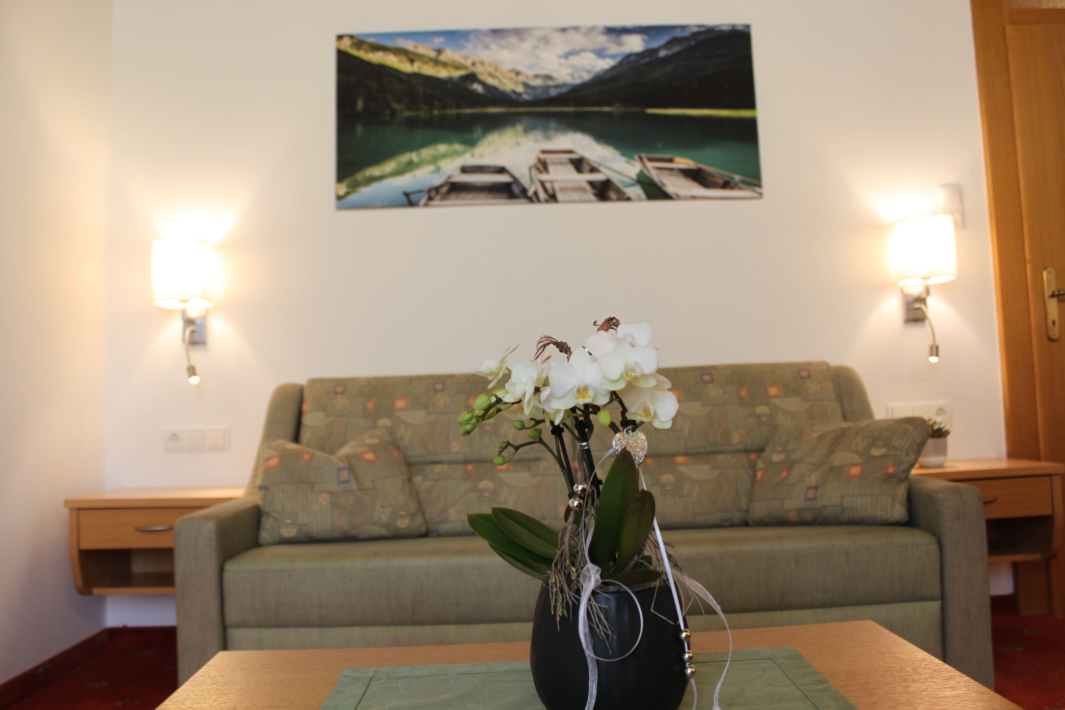 Ein Zimmer mit einer Couch, einem Tisch mit Blumenvase und einem Bild von einem See an der Wand.
