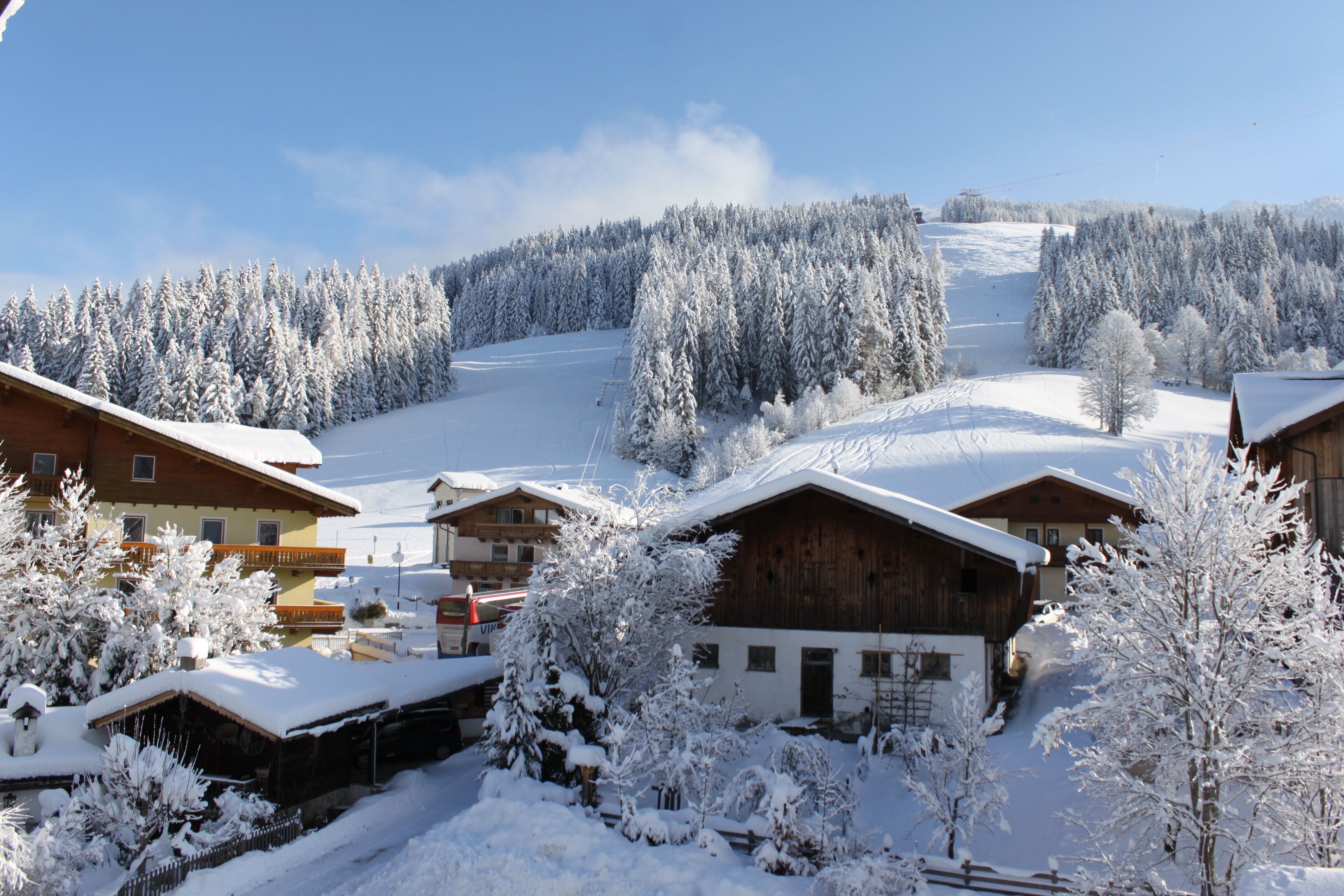 Un pueblo cubierto de nieve con edificios de madera y una pista de esquí al fondo.
