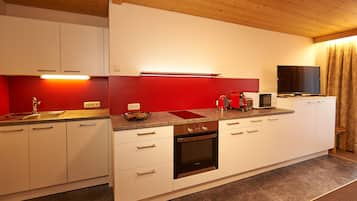 Una cocina moderna con armarios blancos, un salpicadero rojo, horno empotrado y un televisor de pantalla plana.