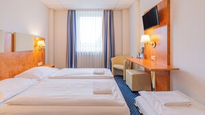 Une chambre d’hôtel avec deux lits, un bureau avec une télévision, une chaise et une fenêtre avec des rideaux.