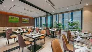 A modern dining area with glass tables, cushioned chairs, and large windows offering a view of greenery. - Grand Cititel Hanoi Hotel & Spa (Hanoi)