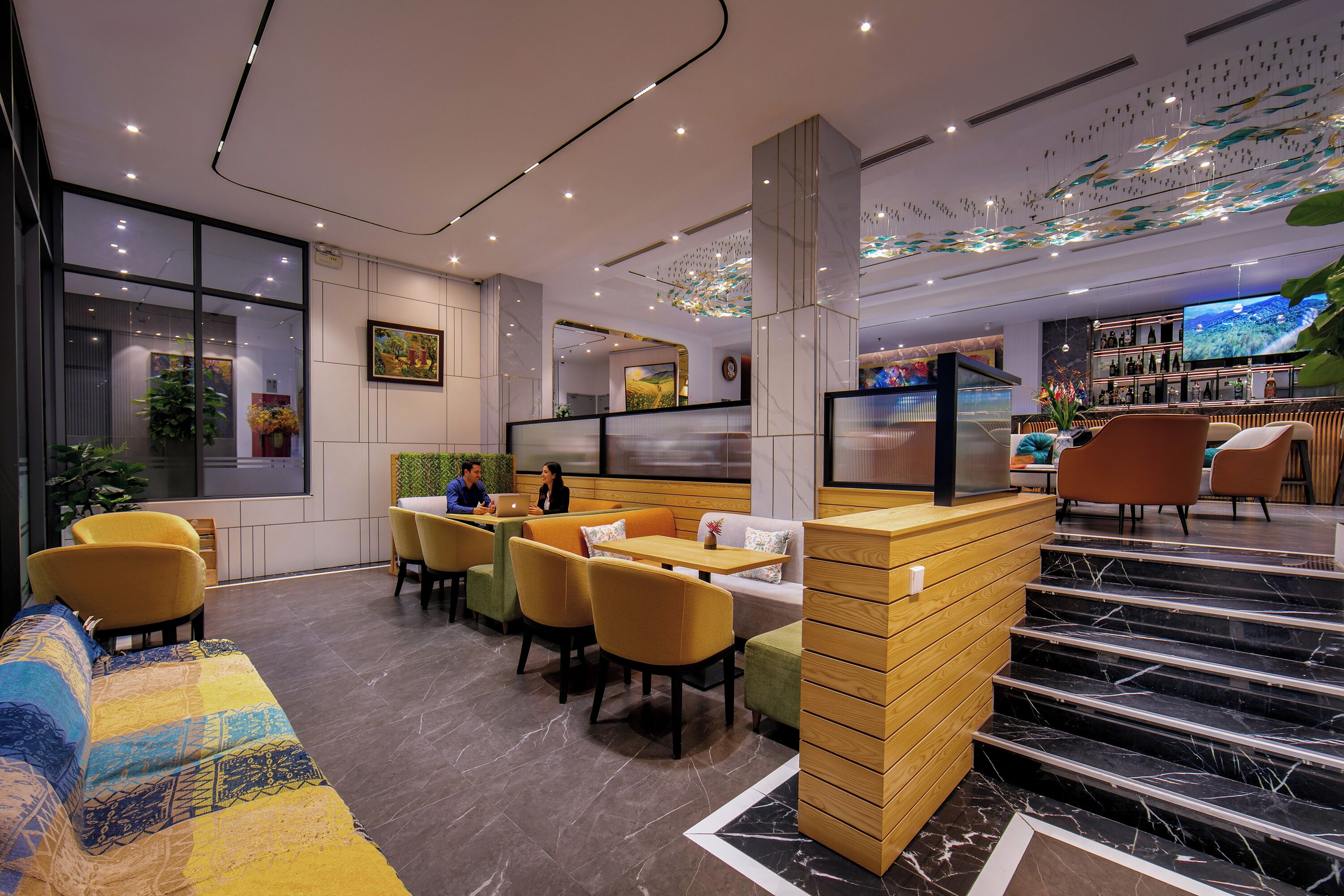 A modern hotel lobby with a seating area, a bar, and a staircase.