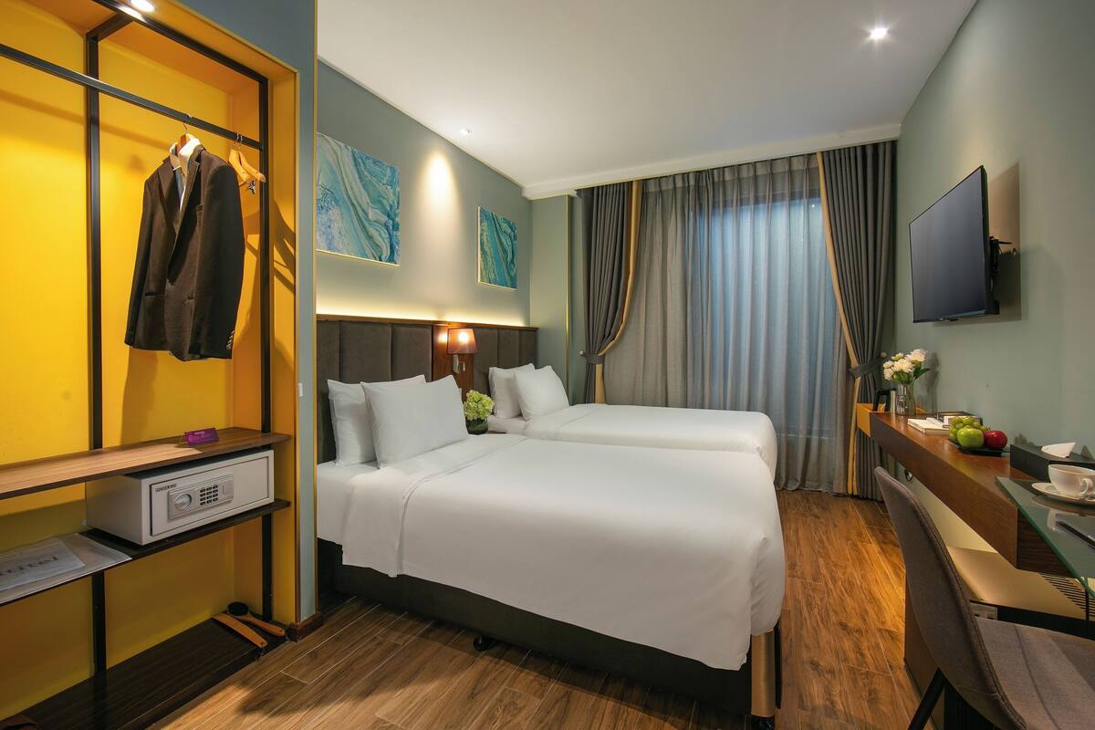 Ett hotellrum med två sängar, ett skrivbord med en stol, en tv och en klädställning.