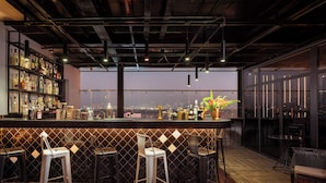 A bar area with a city view, bar stools, and a shelf of bottles. - Grand Cititel Hanoi Hotel & Spa (Hanoi)