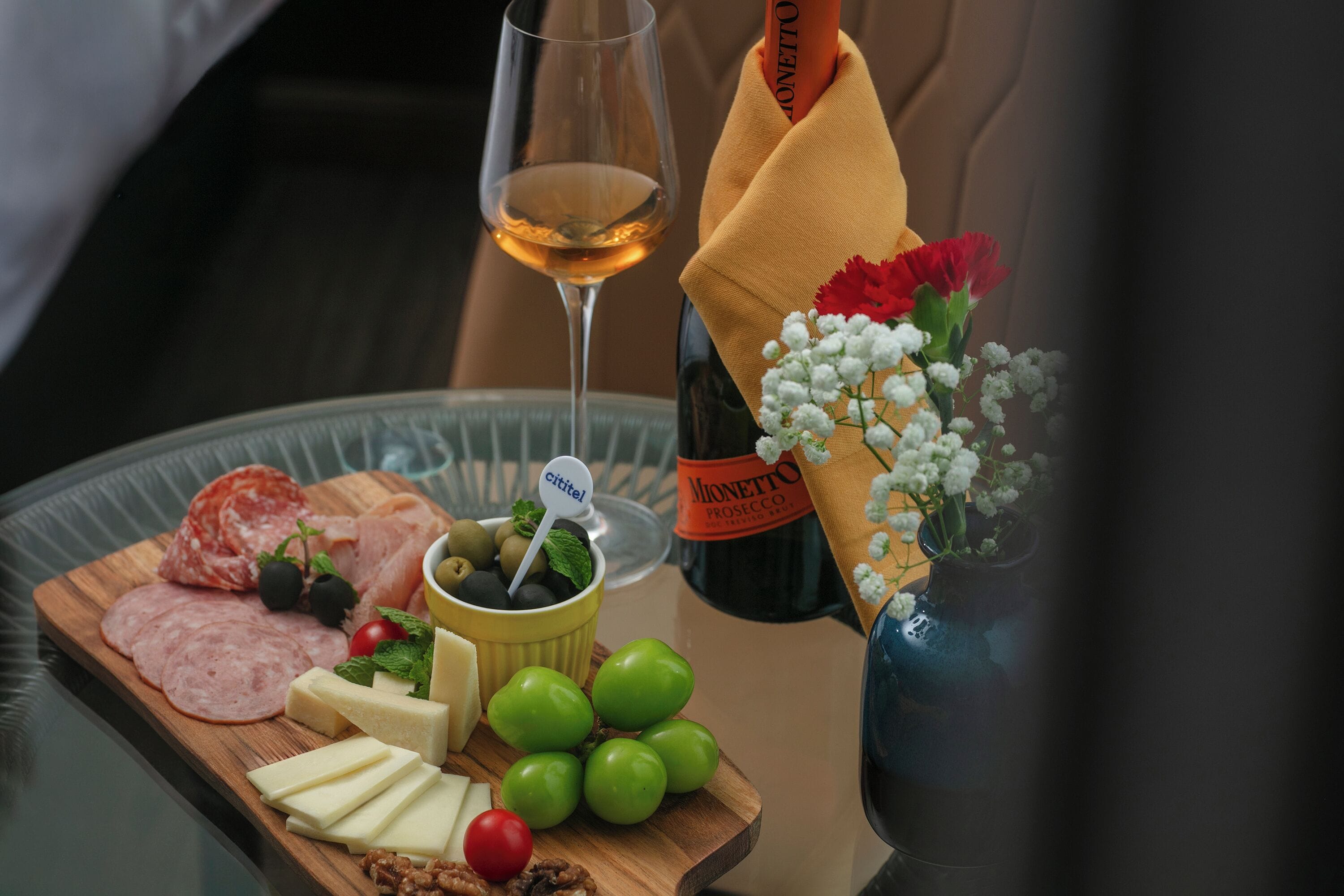 A charcuterie board with various meats, cheeses, and fruits, a bottle of wine, and a vase with flowers.