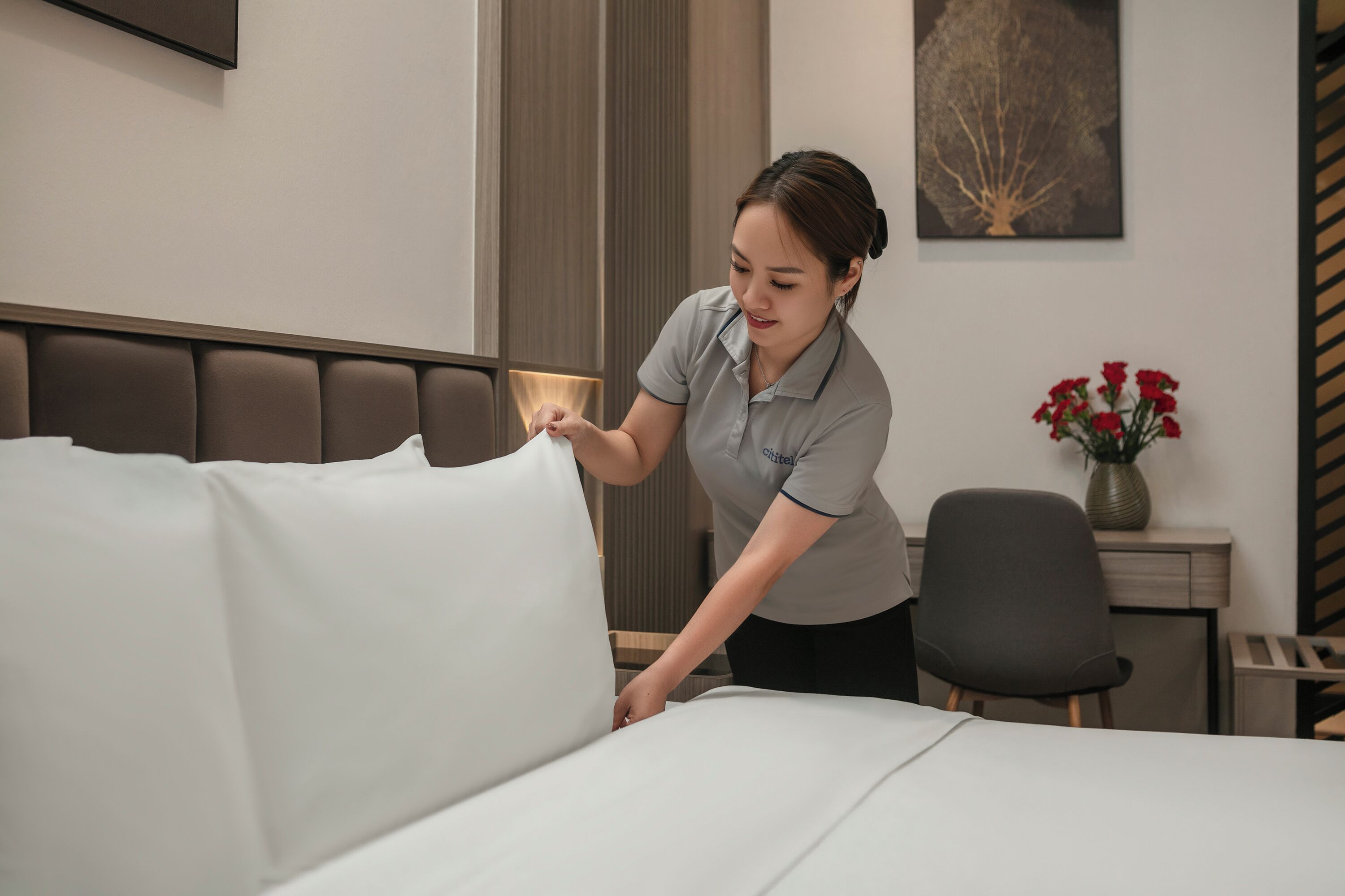 Una habitación de hotel con una cama bien hecha, un escritorio con un florero y una silla.