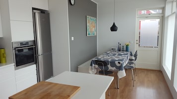 A modern kitchen with a built-in oven and refrigerator, a dining table with a patterned tablecloth, and a gray wall with a map.