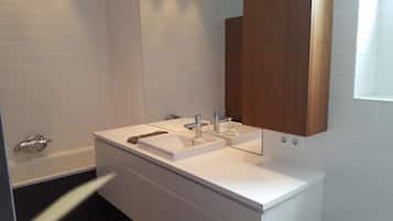 A modern bathroom with white tiled walls, a white vanity with two sinks, a wooden cabinet above the mirror, and a towel rack.
