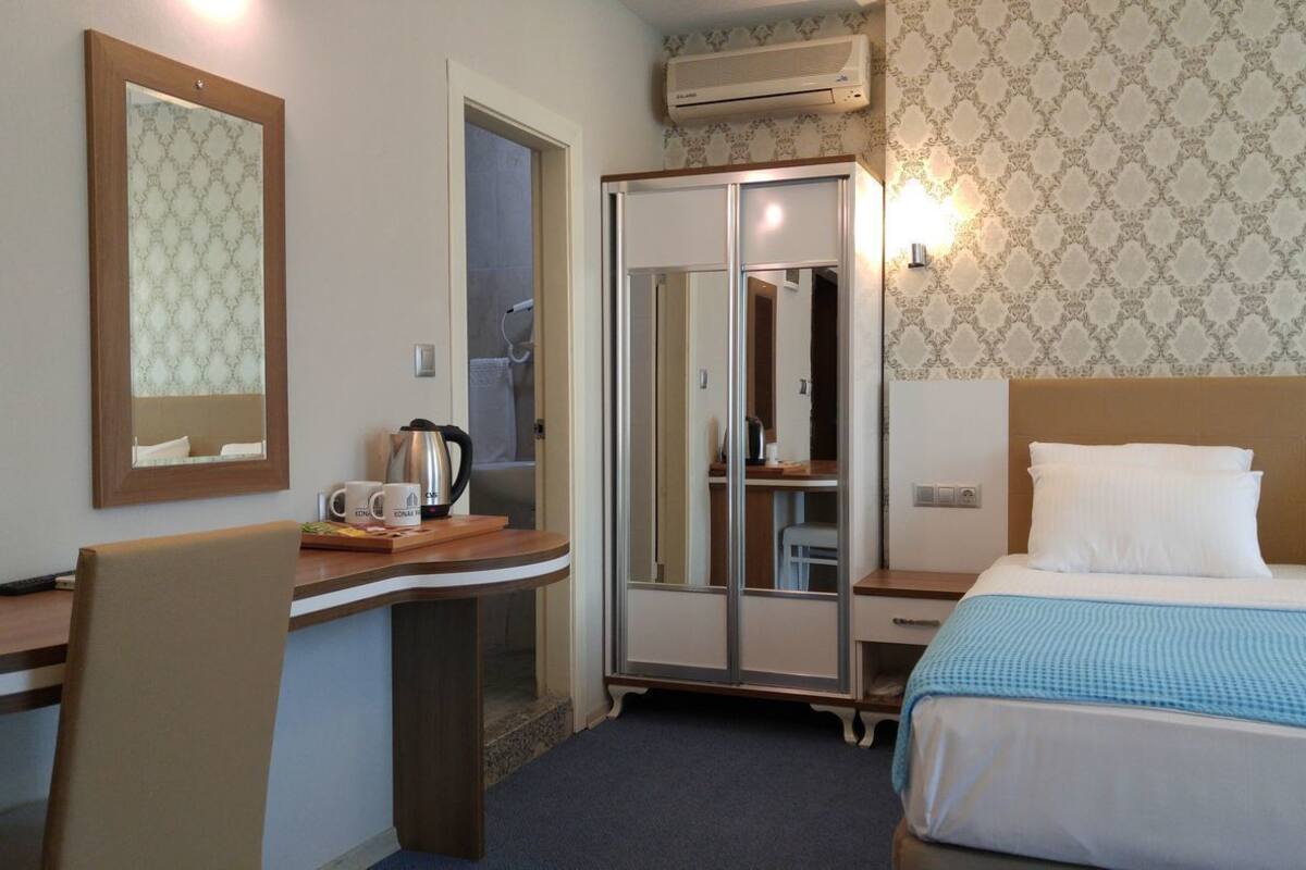 A hotel room with a bed, a desk, a chair, a wardrobe, and a mirror.