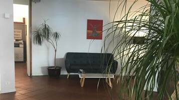 Un salon avec un canapé de couleur sombre, une plante en pot et un tableau accroché au mur.