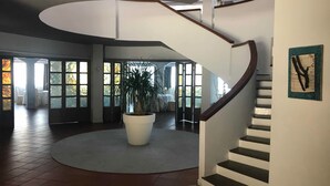 A spacious interior with a central potted plant, a curved staircase, and large windows allowing natural light. - Baia dell'est (Montauro)