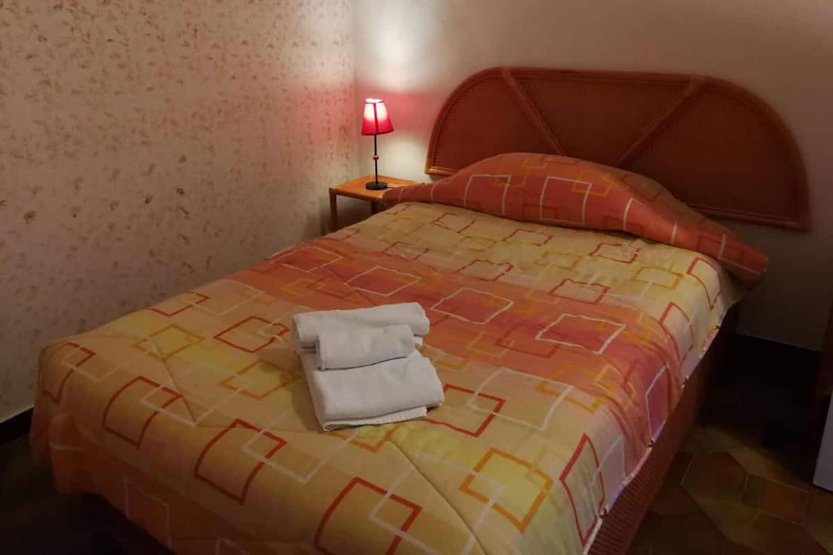 A neatly made bed with a patterned bedspread, a pillow, and a folded towel on the bed.