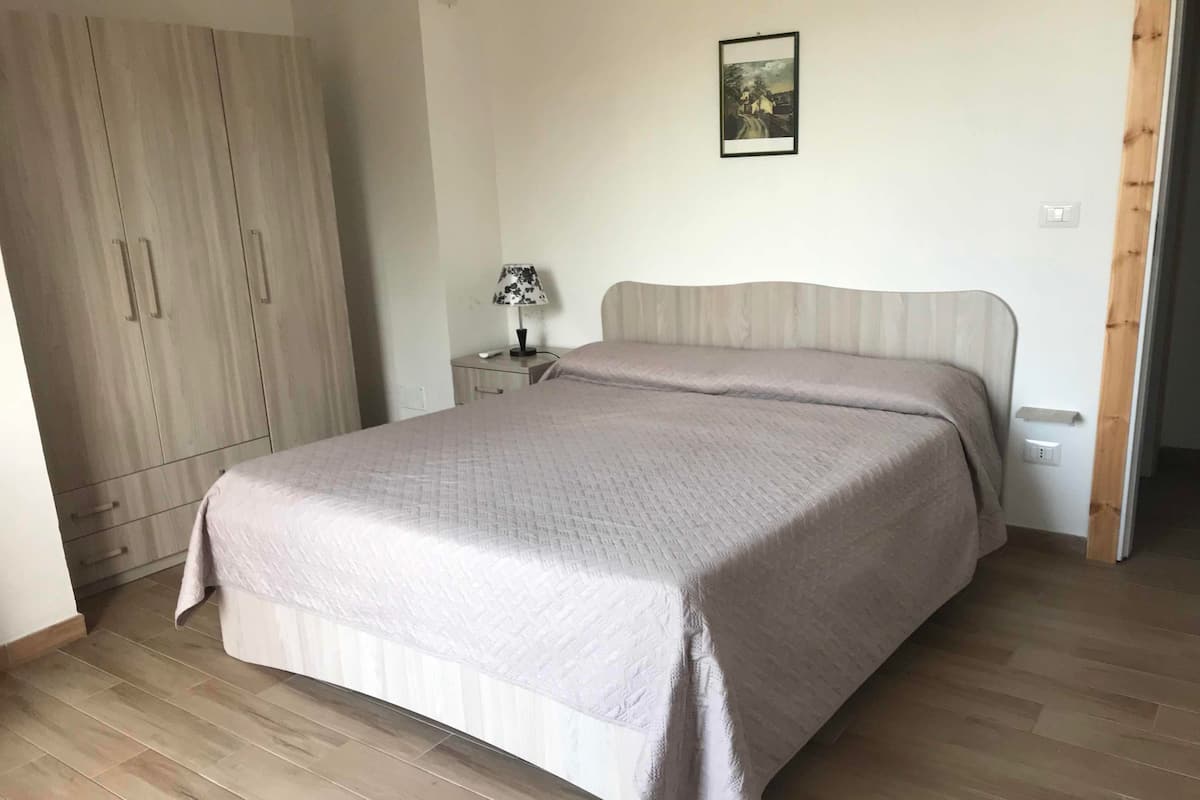 A bedroom with a bed, a nightstand, a lamp, a wardrobe, and a picture on the wall.