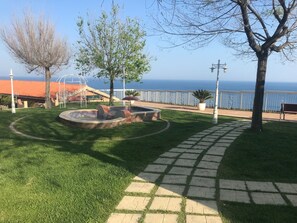 A park with a fire pit, a paved walkway, and a view of the sea.