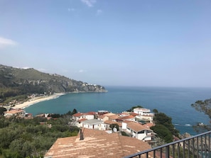 A coastal town with terracotta-roofed buildings, a beach, and a clear view of the sea.