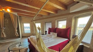 Un dormitorio con una cama grande, una silla colgante y vistas al exterior por una ventana.