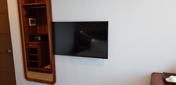 Televisor de pantalla plana montado en una pared blanca, con un estante de madera debajo que contiene un altavoz y un cuadro enmarcado.