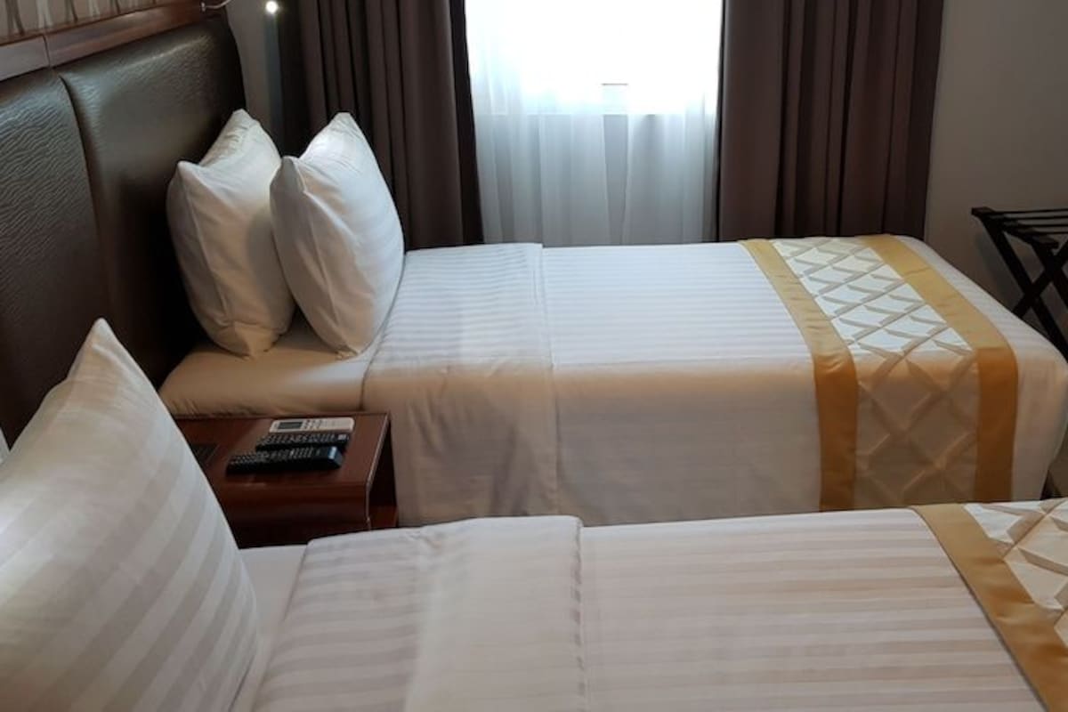 A hotel room with two beds, a nightstand, and a small table.