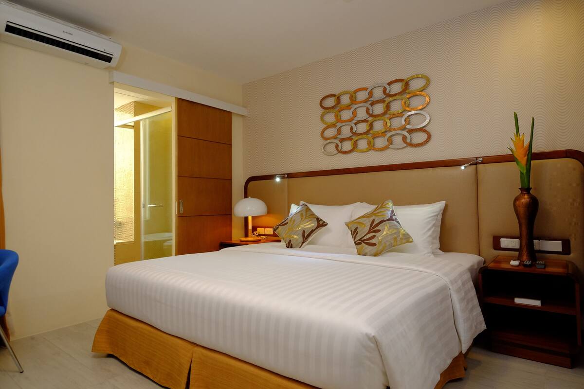 Une chambre d’hôtel avec un grand lit, une table de chevet avec une lampe, un élément décoratif mural et une table de nuit en bois.