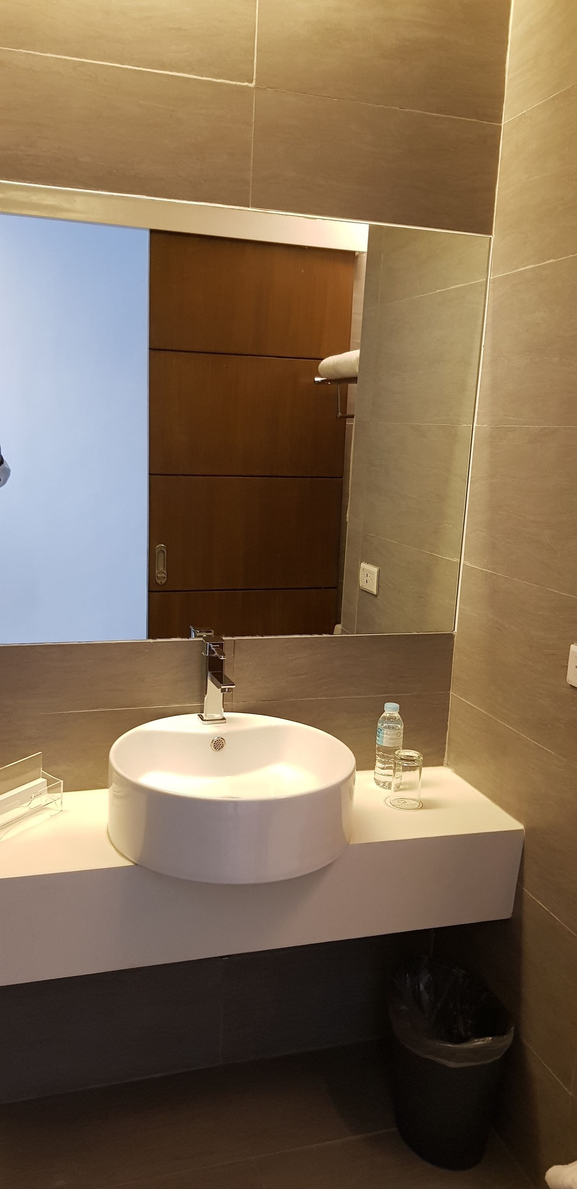 A modern bathroom with a round sink, a mirror, and a wooden door.