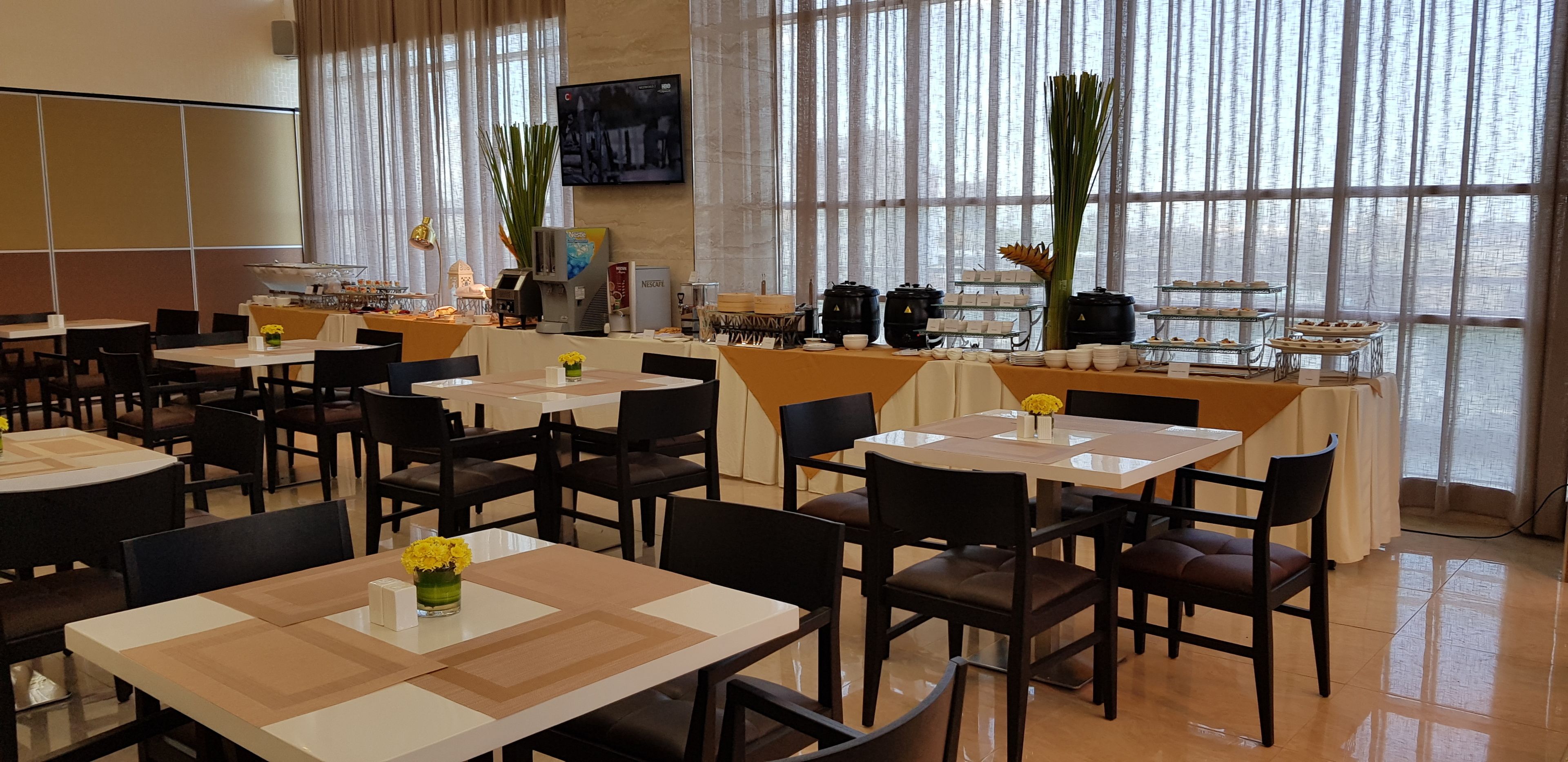 Un espace repas comprenant plusieurs tables et chaises, un coin café et un écran de télévision.