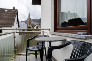 Un balcón con dos sillas y una mesita, con vistas a una iglesia y edificios residenciales.