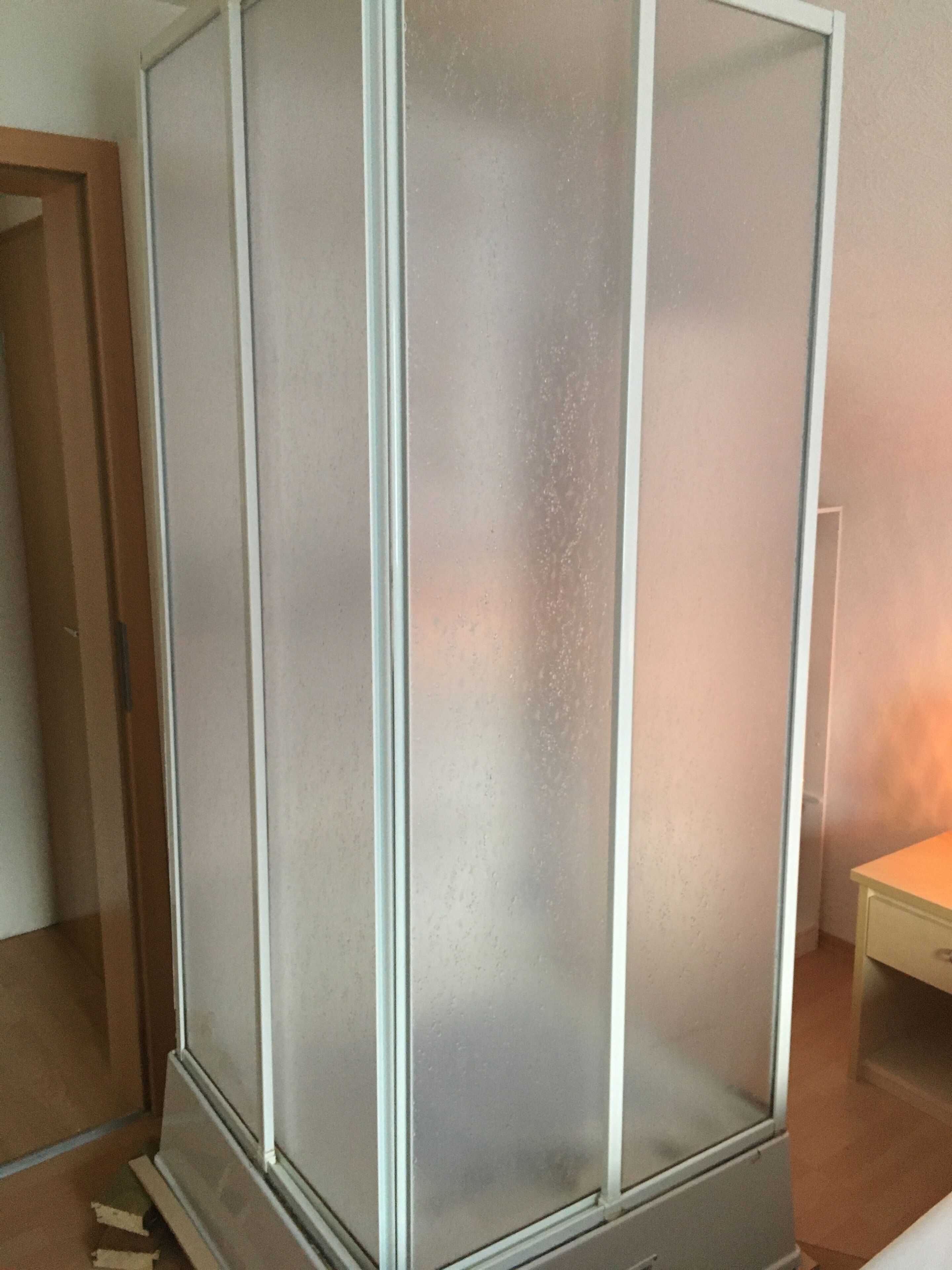 Una habitación con un amplio panel de vidrio esmerilado, una puerta de madera y una pequeña mesa.