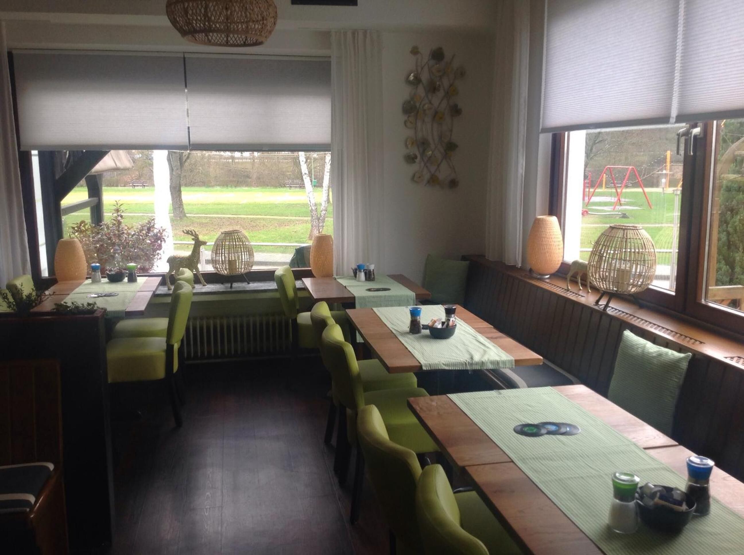 A dining area with a long table, green chairs, and a view of a garden through large windows.