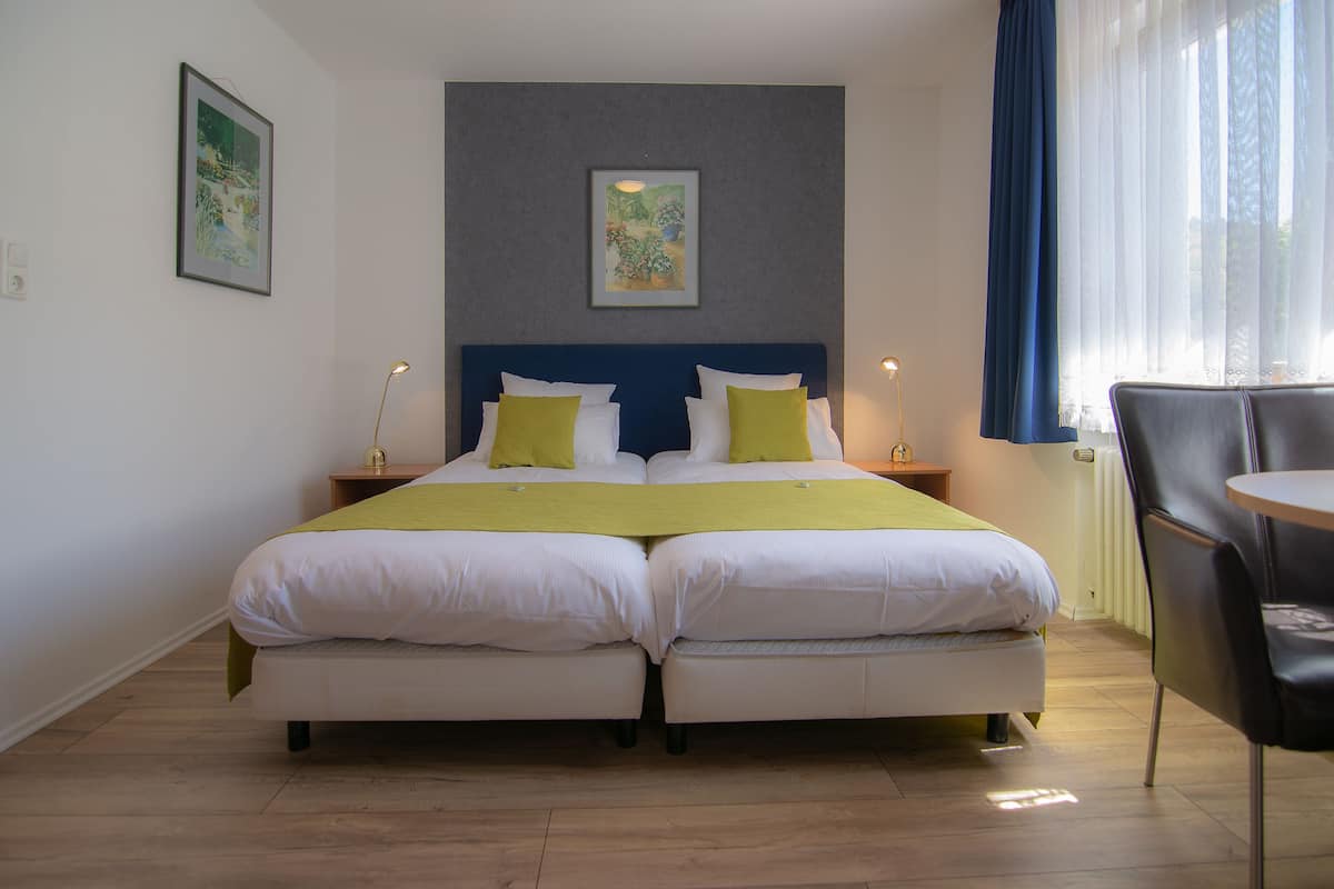 A double bed with white and yellow bedding, a blue headboard, and two bedside tables with lamps.