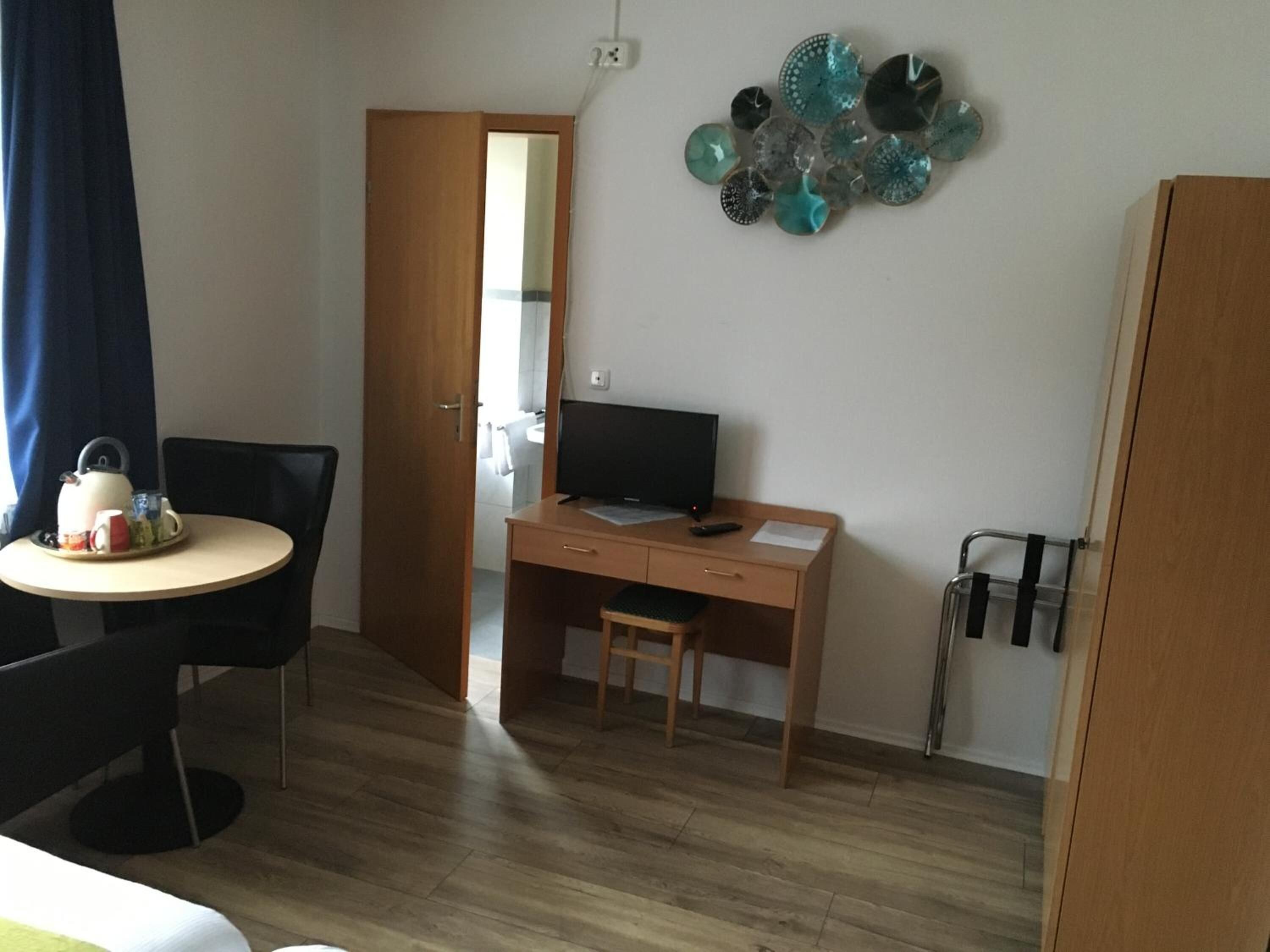 Una habitación pequeña y ordenada con un escritorio de madera, una silla, un televisor y una mesa de comedor con una bandeja de té y tazas.