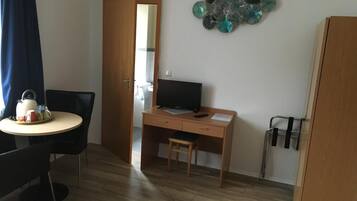 Una habitación pequeña y ordenada con un escritorio de madera, una silla, un televisor y una mesa de comedor con una bandeja de té y tazas.