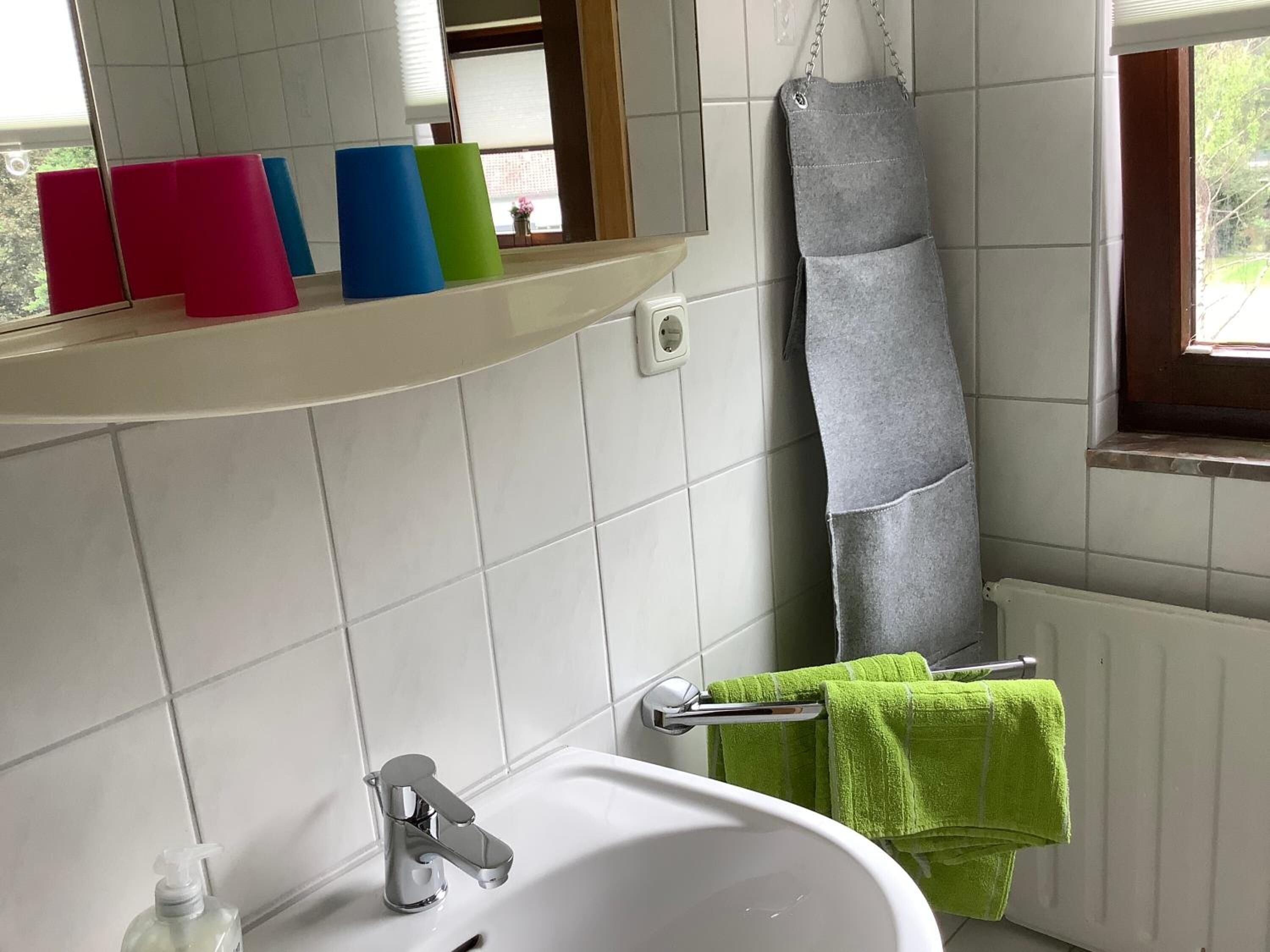 Un ba ño con un lavamanos blanco, un espejo y una repisa con toallas de colores.
