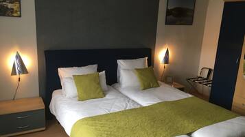 Una cama doble con ropa de cama blanca y verde, dos lámparas de noche, una mesita de noche, una silla y un cuadro en la pared.