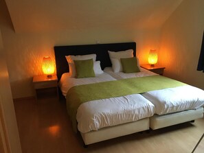Una cama doble con una manta verde, ropa de cama blanca y dos lámparas de noche.