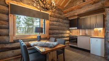Interior de una cabaña de troncos con comedor, cocina y un ventanal con vistas a un bosque.
