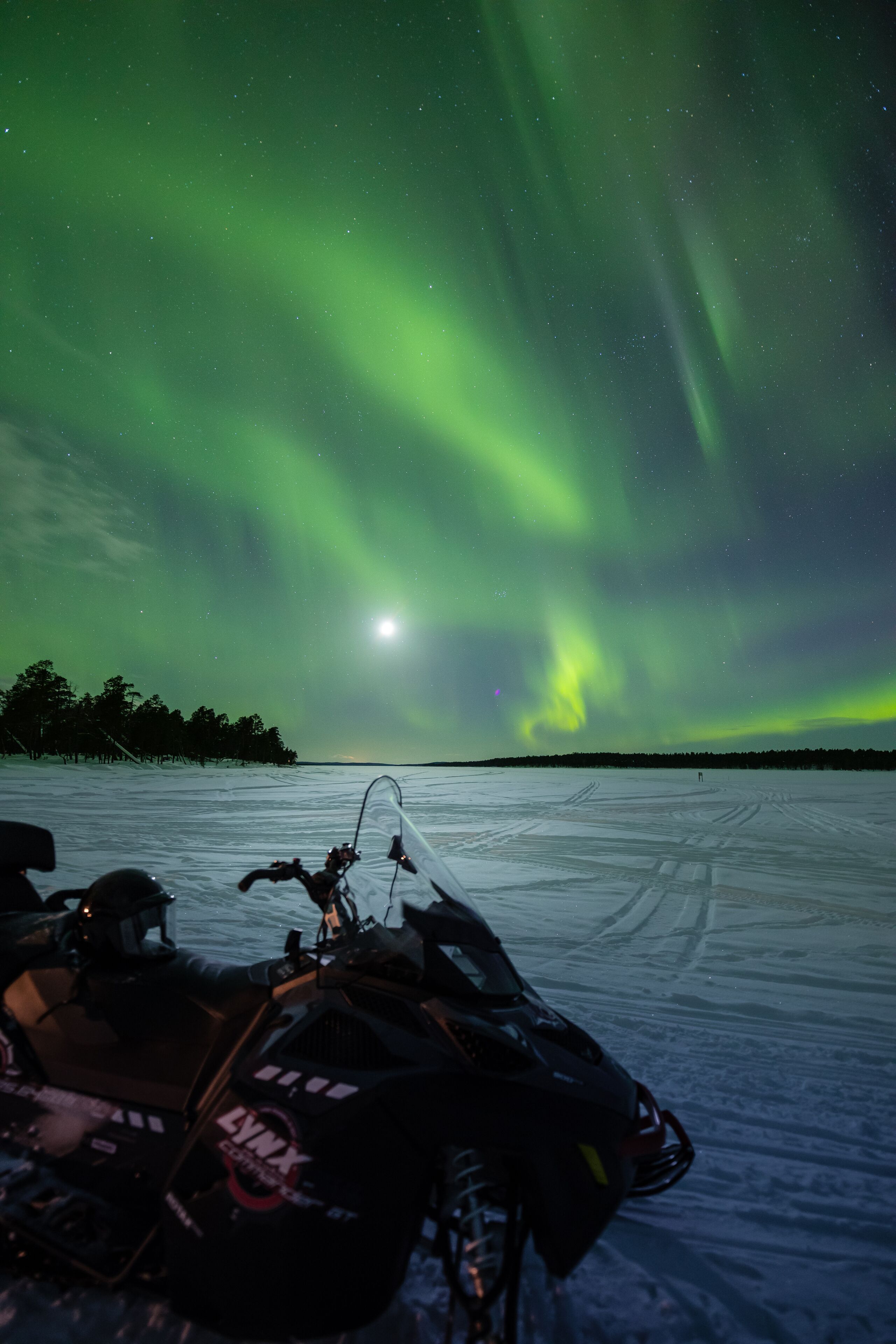 A snow-covered landscape with a snowmobile parked in the foreground and a visible moon in the sky.