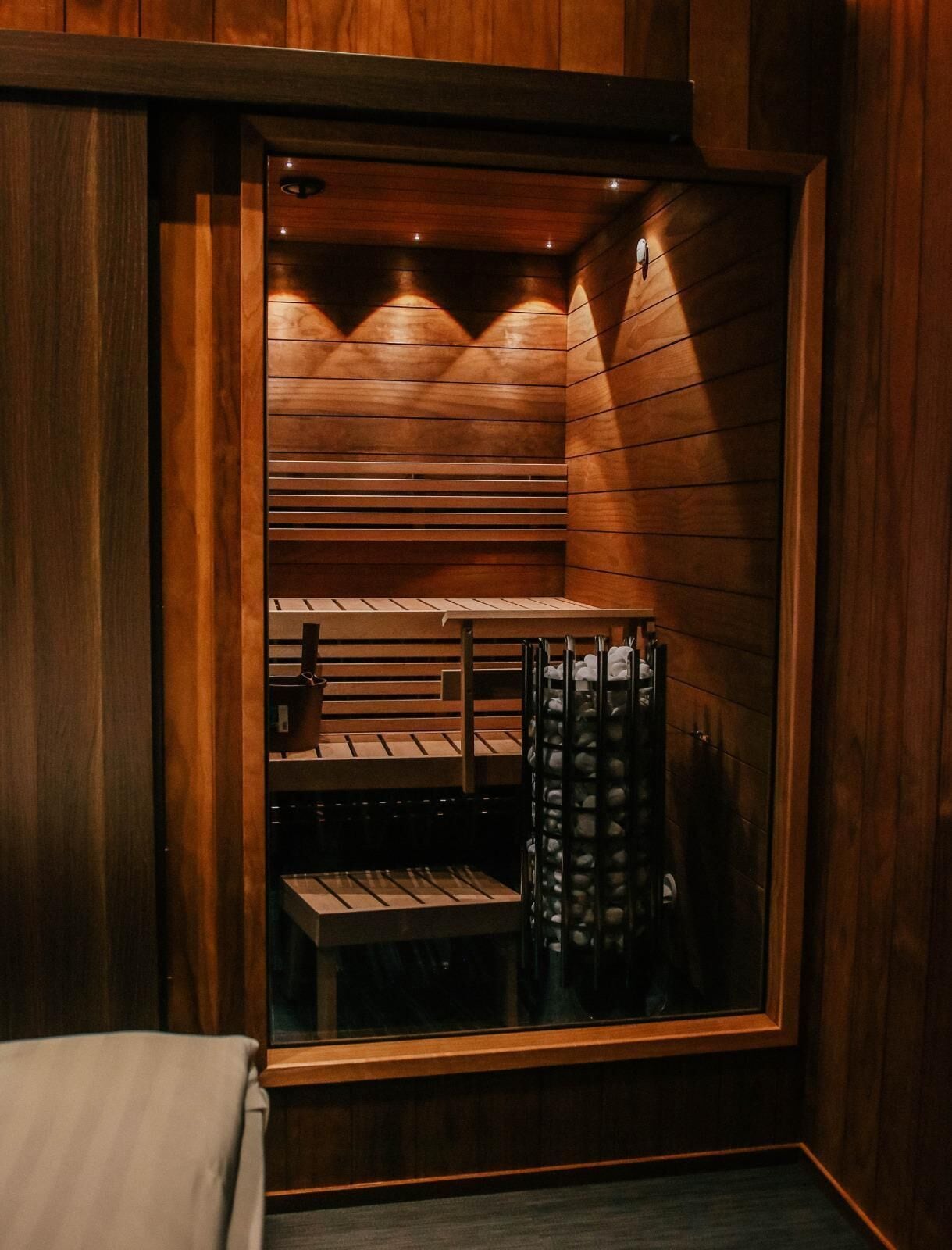 Una sauna con paredes y bancos de madera, una puerta de vidrio y un perchero para toallas.